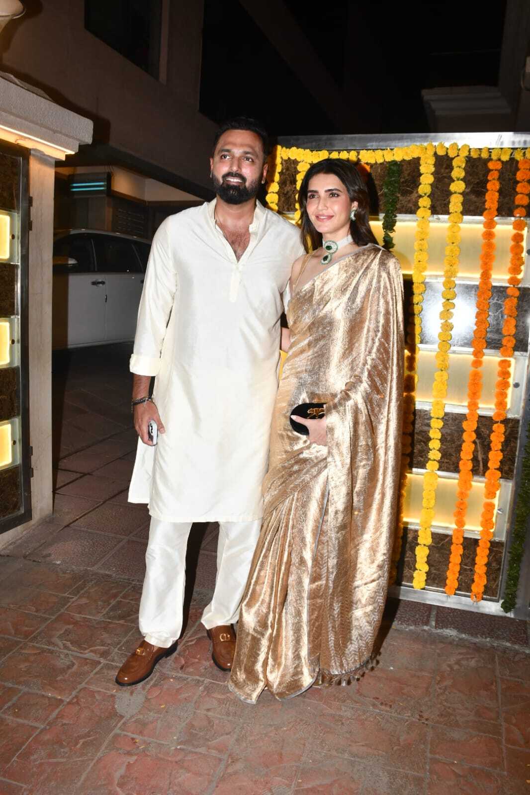 Karishma Tanna wore a golden shimmery saree made of tissue fabric and accessorized it with a large emerald green choker necklace and matching earrings. Varun Bangera chose an ivory-colored kurta-pajama.